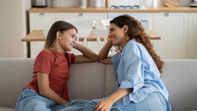 A mother and daughter sitting on their living room couch having a conversation.
