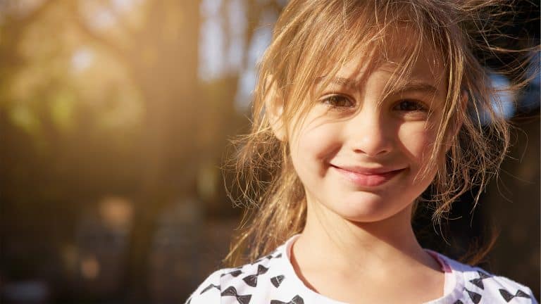 Photo of a shy young girl looking directly at the camera smiling.