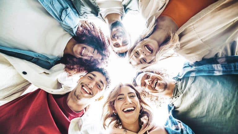 Happy group of friends hugging together in a circle - Multiracial community of young people smiling at camera - Community concept.