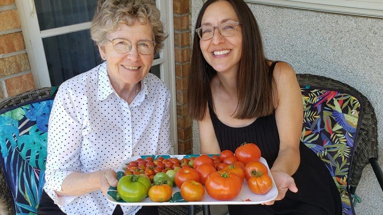 Mother and daughter sitting together holding tray of tomatoes