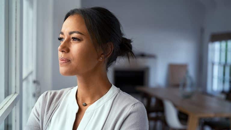 A pensive woman at home worried about change in her life looking out a window.